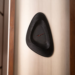 Black wall clock with wavy design on a beige wall